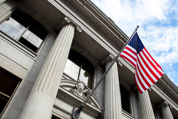 american-flag-flying-over-government-building-in-city-blue-sky-and-clouds1263450790 Stone granite official government building in city with American flag waving and flying in the wind, looking up, outside, judicial, freedom, civil courts, columns, criminal justice, law