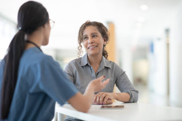 A female doctor of East Indian decent meets with her mixed race senior patient.  The doctor is wearing scrubs and using her hands to explain the results to the patient.  The patient is wearing casual clothing and smiling as she listens to the doctor.